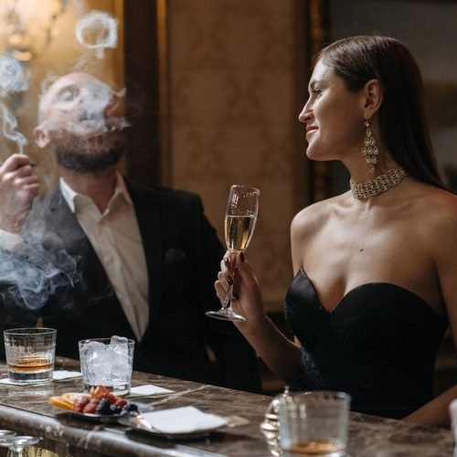 A Woman Holding a Champagne Glass Beside a Man Smoking